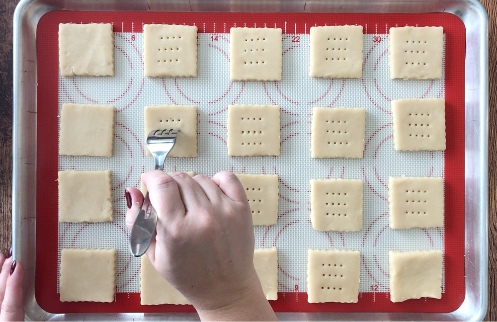 Fork poking holes in tops of shortbread cookie dough pieces on a baking sheet