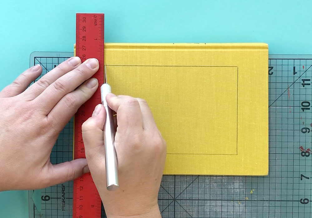 Hands using exacto knife to cut rectangle window from book cover