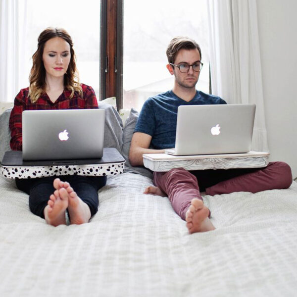 People on a bed using laptop desks.