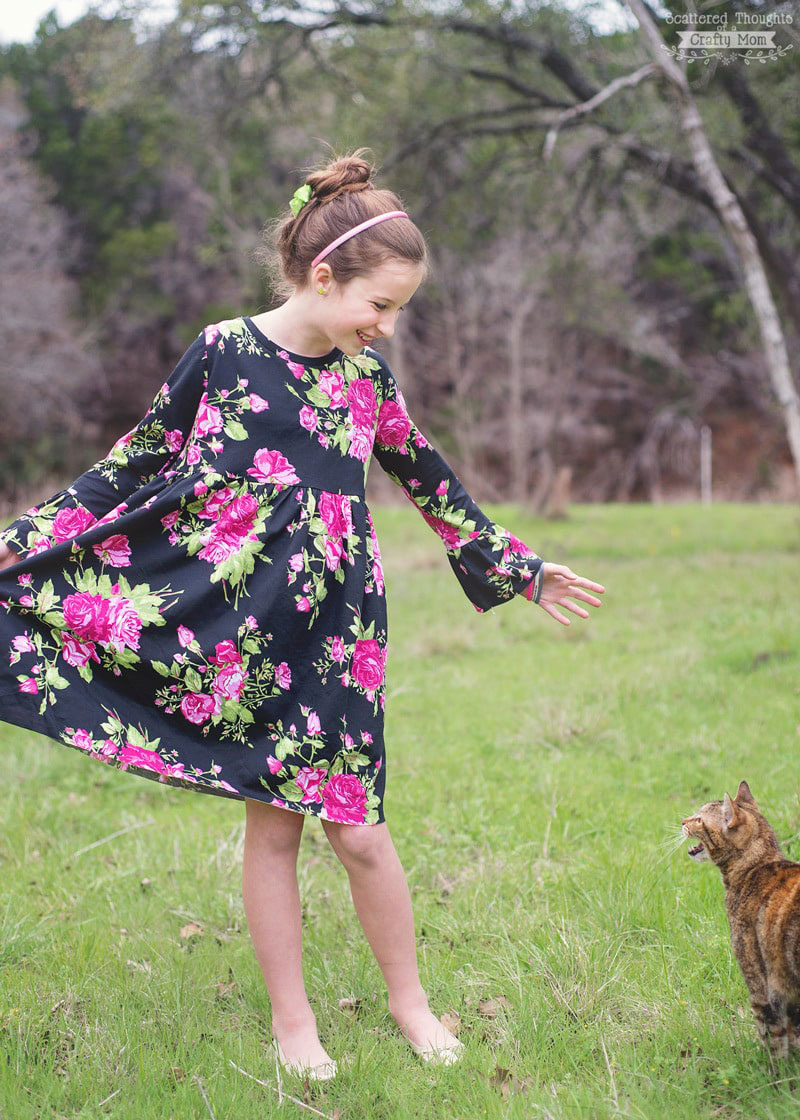 A little girl that is standing in the grass wearing a long sleeve dress