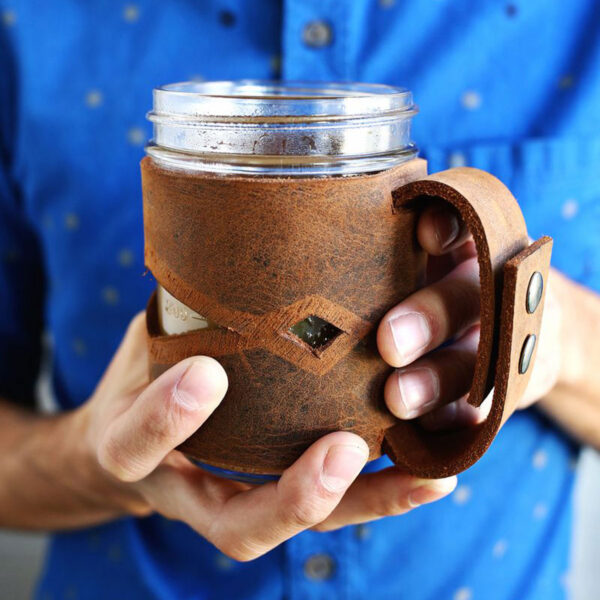 Man holding mason jar in a leather sleeve.