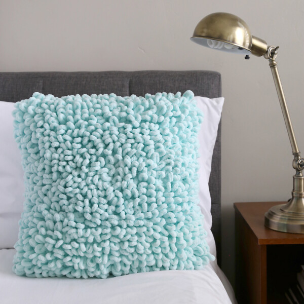 A throw pillow with a soft loopy texture on a bed