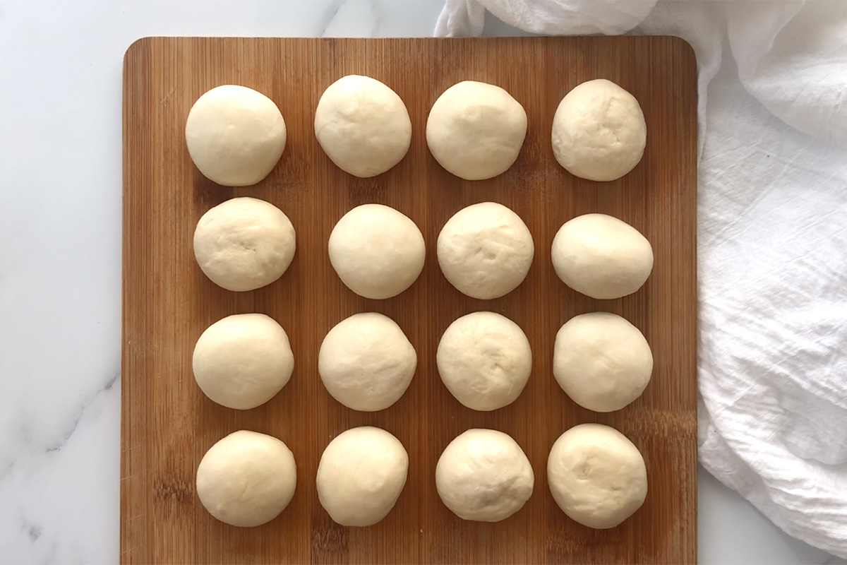 16 frozen dinner roll dough balls on a wood cutting board