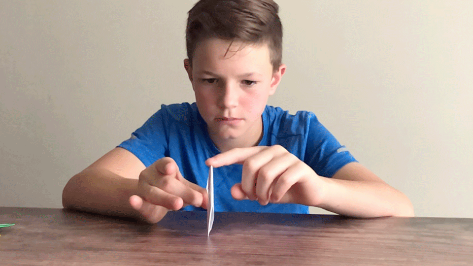 Animated gif of a boy flicking a folded paper football