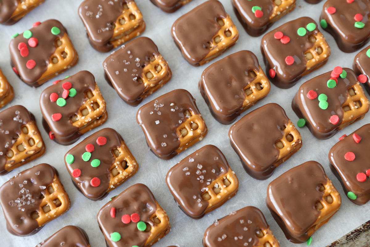 Square pretzels filled with caramel and dipped in chocolate, some decorated with sprinkles