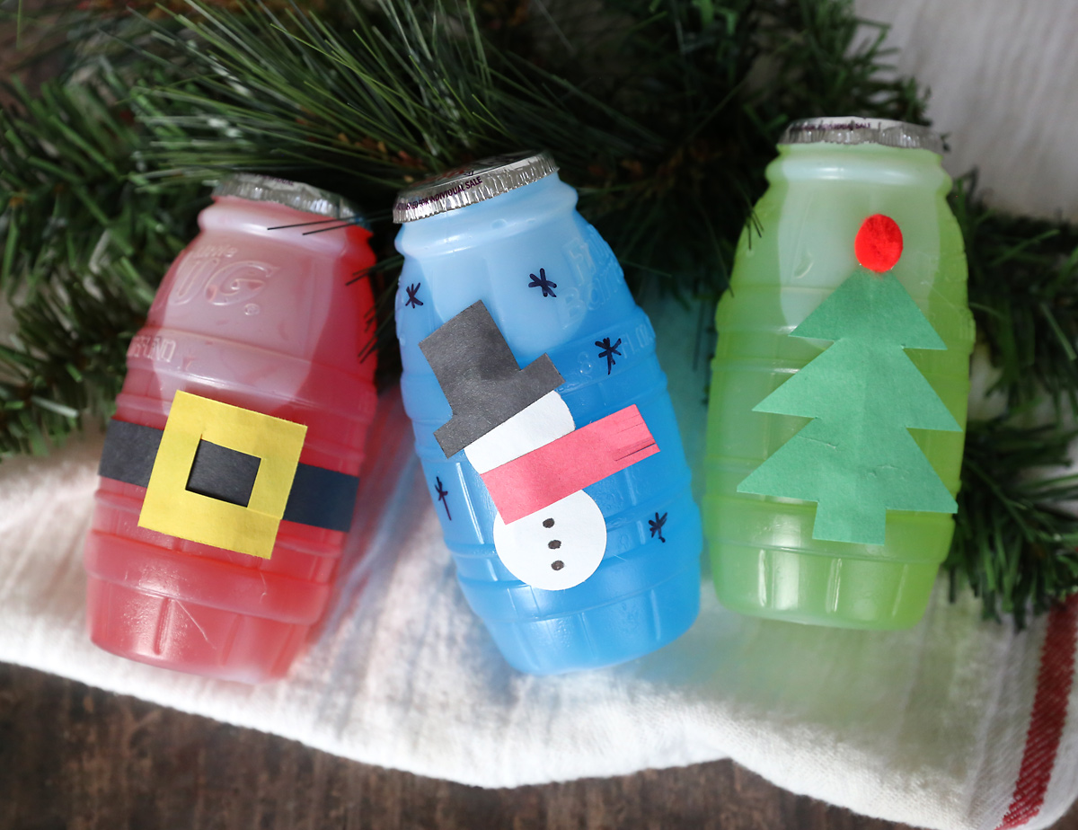 Juice treat jugs decorated for Christmas: Santa\'s belt on the red jug, paper snowman on the blue jug, Christmas tree on the green jug