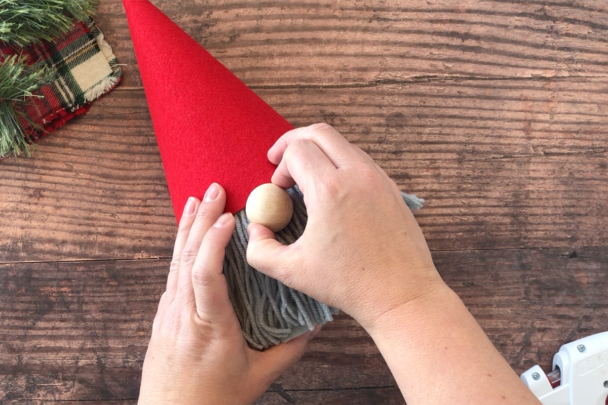 Hand holding wood bead that\'s been glued on for the gnome\'s nose