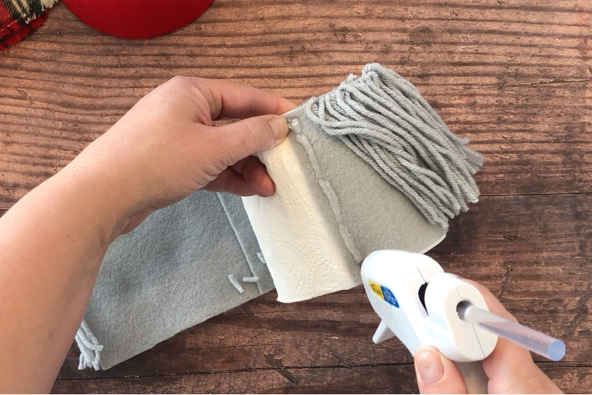 Hand hot gluing the yarn covered felt around a roll of toilet paper