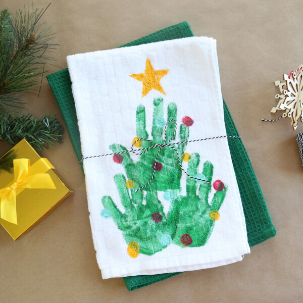 Kitchen towel with Christmas tree made from handprints on it, tied with twine as a gift