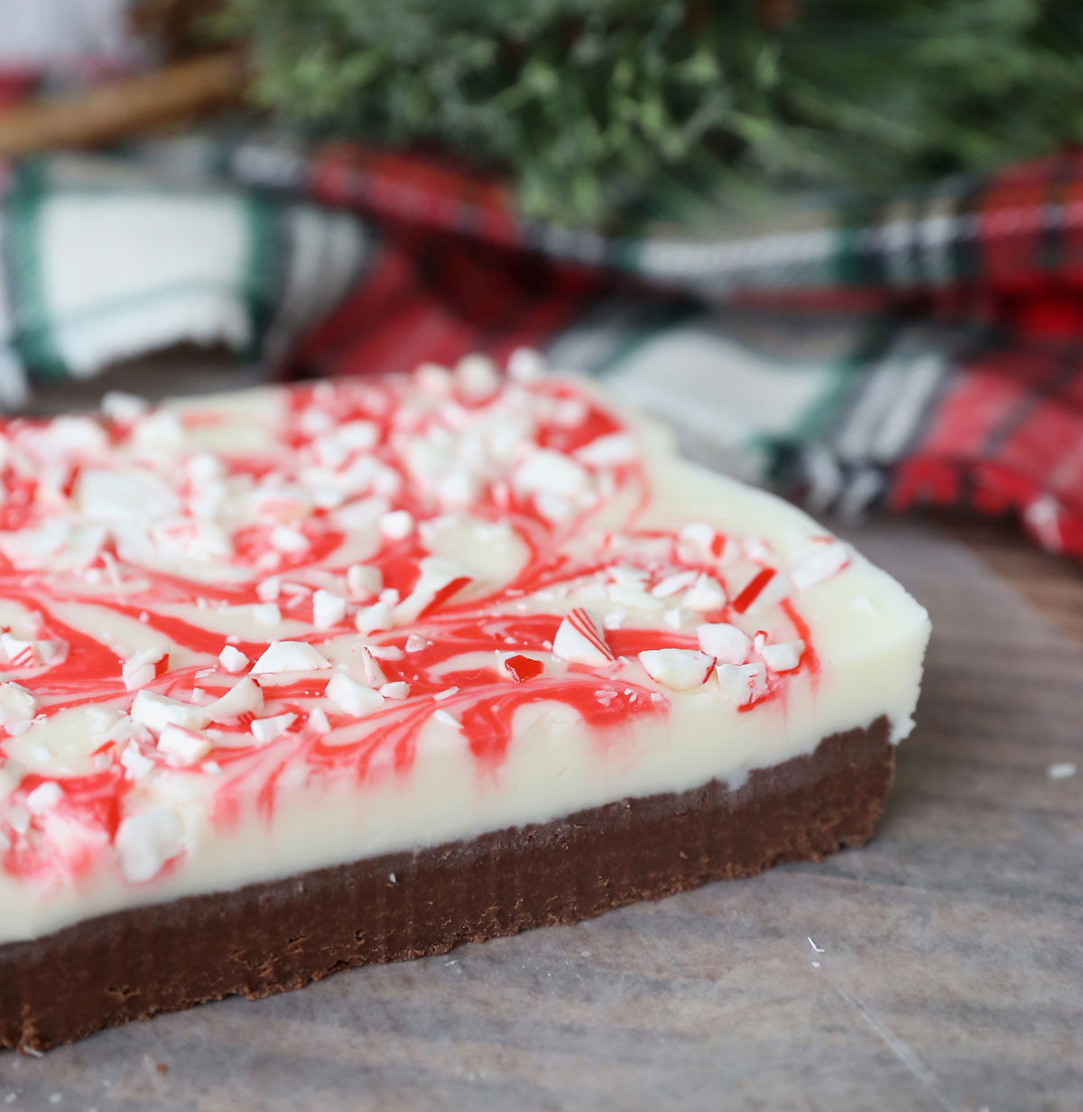 Peppermint bark fudge on a table; bottom layer is chocolate and top layer is white and red peppermint bark