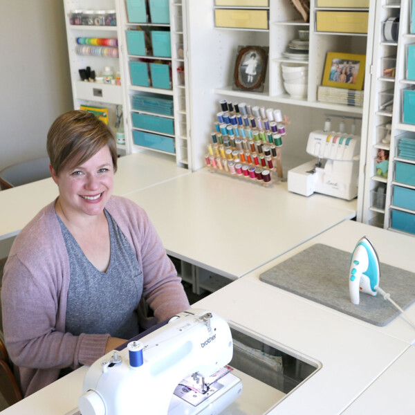 A woman sitting at a table in front of a DreamBox craft storage system with sewing machine table