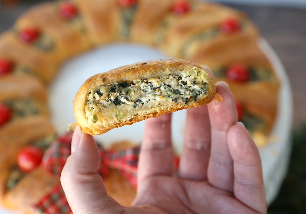Hand holding a slice of spinach dip crescent wreath