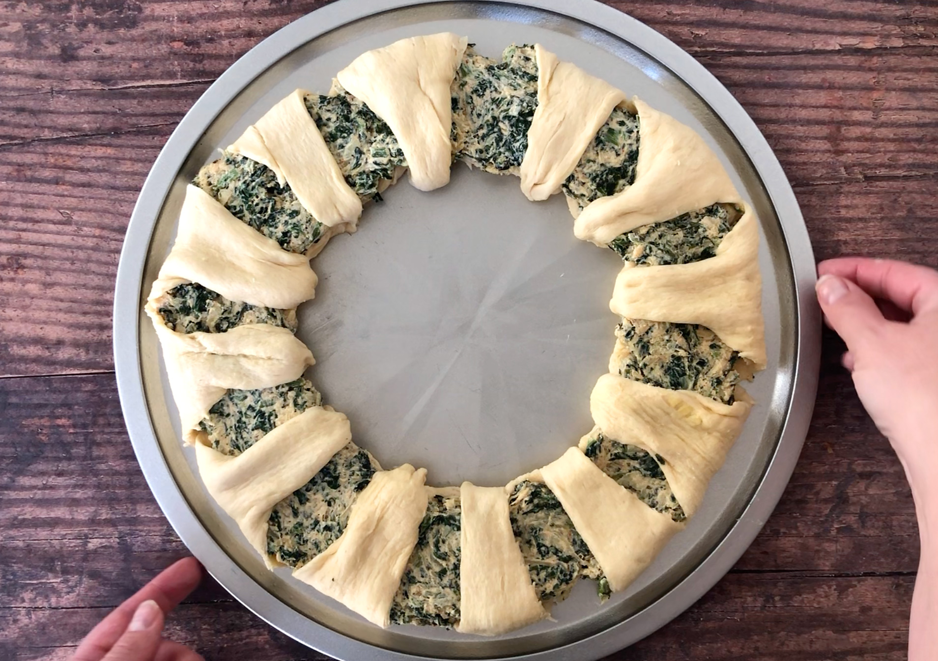 Raw crescent dough slices arranged in a wreath shape filled with spinach dip on a pizza pan