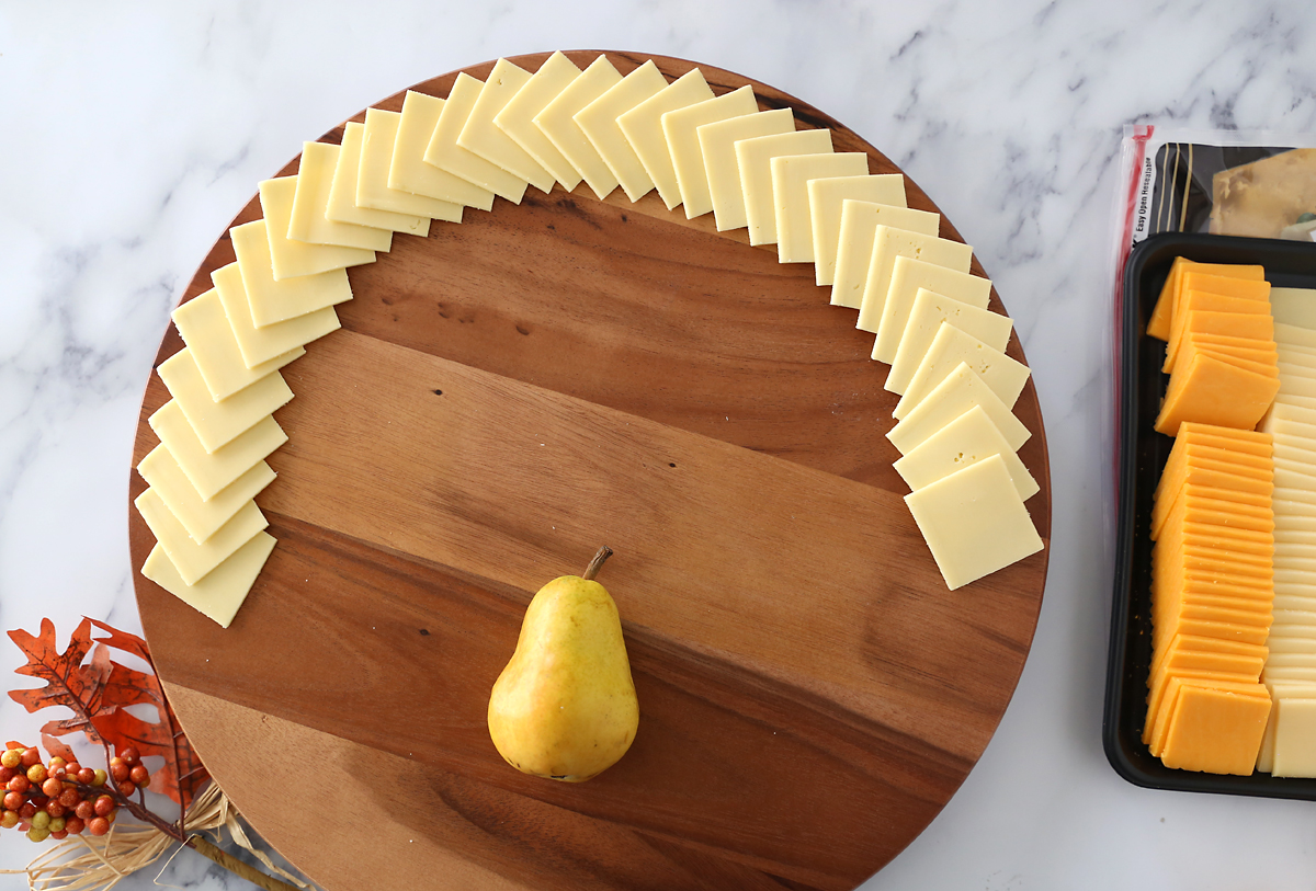 Circular cutting board with pear in bottom middle and white cheese slices fanned around the top two thirds of the edge