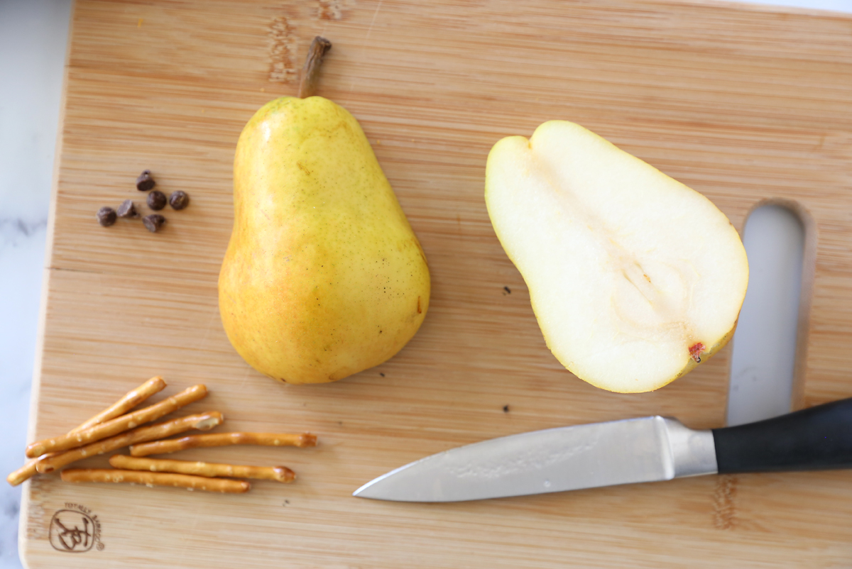 Pear sliced in half from top to bottom with mini chocolate chips and pretzel sticks