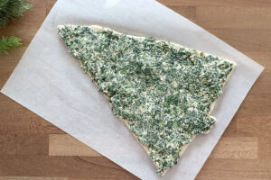 Spinach dip spread across pizza dough triangle.
