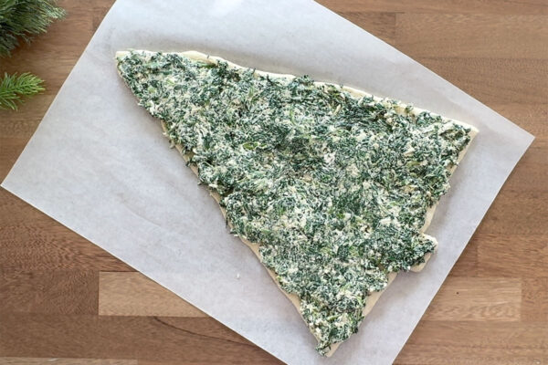 Spinach dip spread across pizza dough triangle.