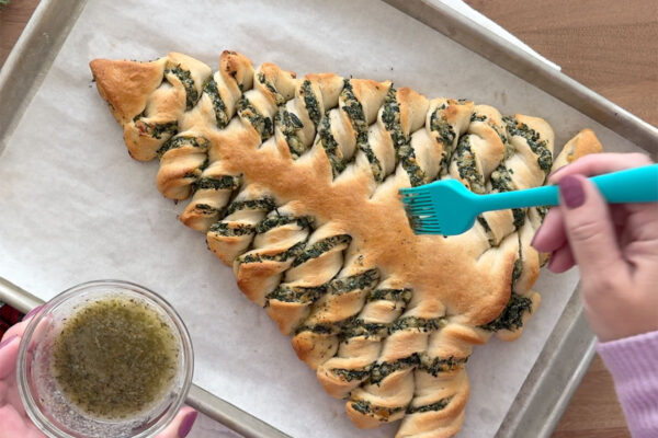 Brushing Christmas tree breadsticks with melted butter.