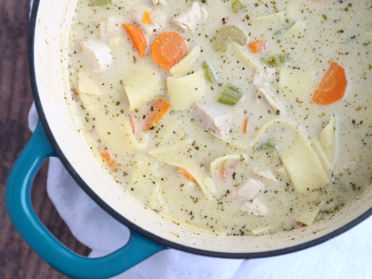 A pot of creamy chicken noodle soup with carrots and celery