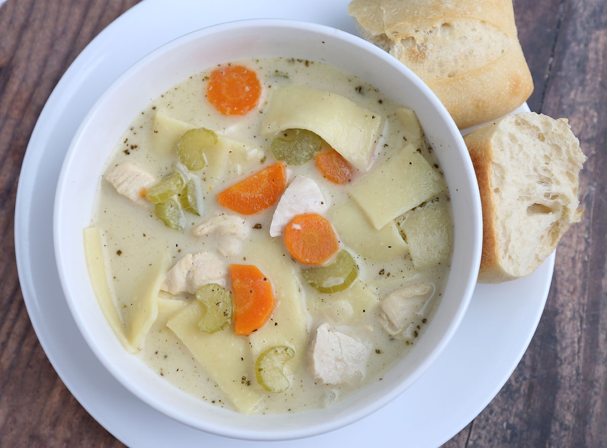 A bowl of creamy chicken noodle soup with carrots and celery and bread roll