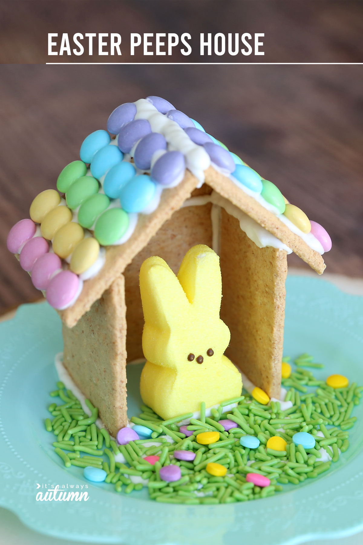 Easter gingerbread house made from graham crackers with Easter M&Ms decorating the roof, with an Easter bunny peep inside