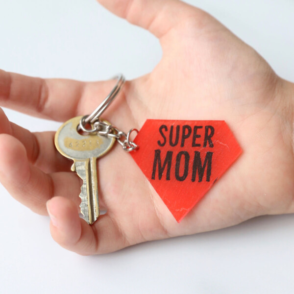 A hand holding a key and Super Mom keychain
