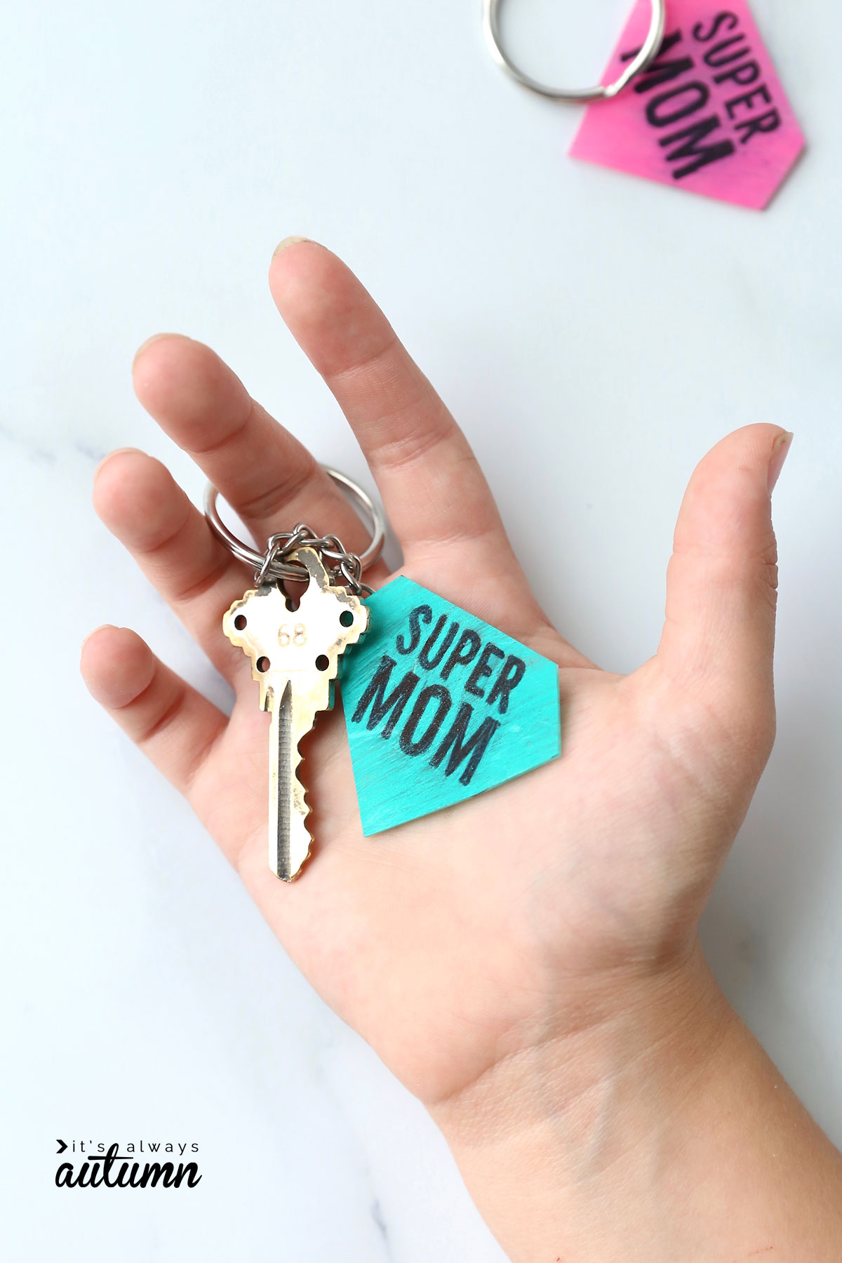 Hand holding a key on a keychain that says supermom