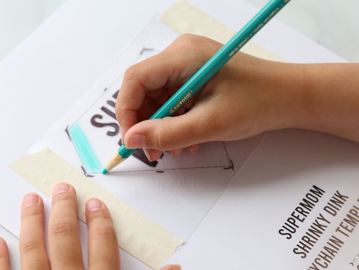Hand using teal colored pencil to color in keychain on shrinky dink paper