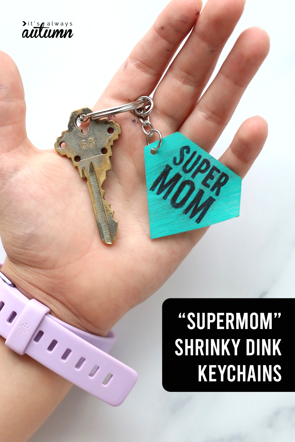 A hand holding a key and a shrinky dink keychain that says \"supermom\"