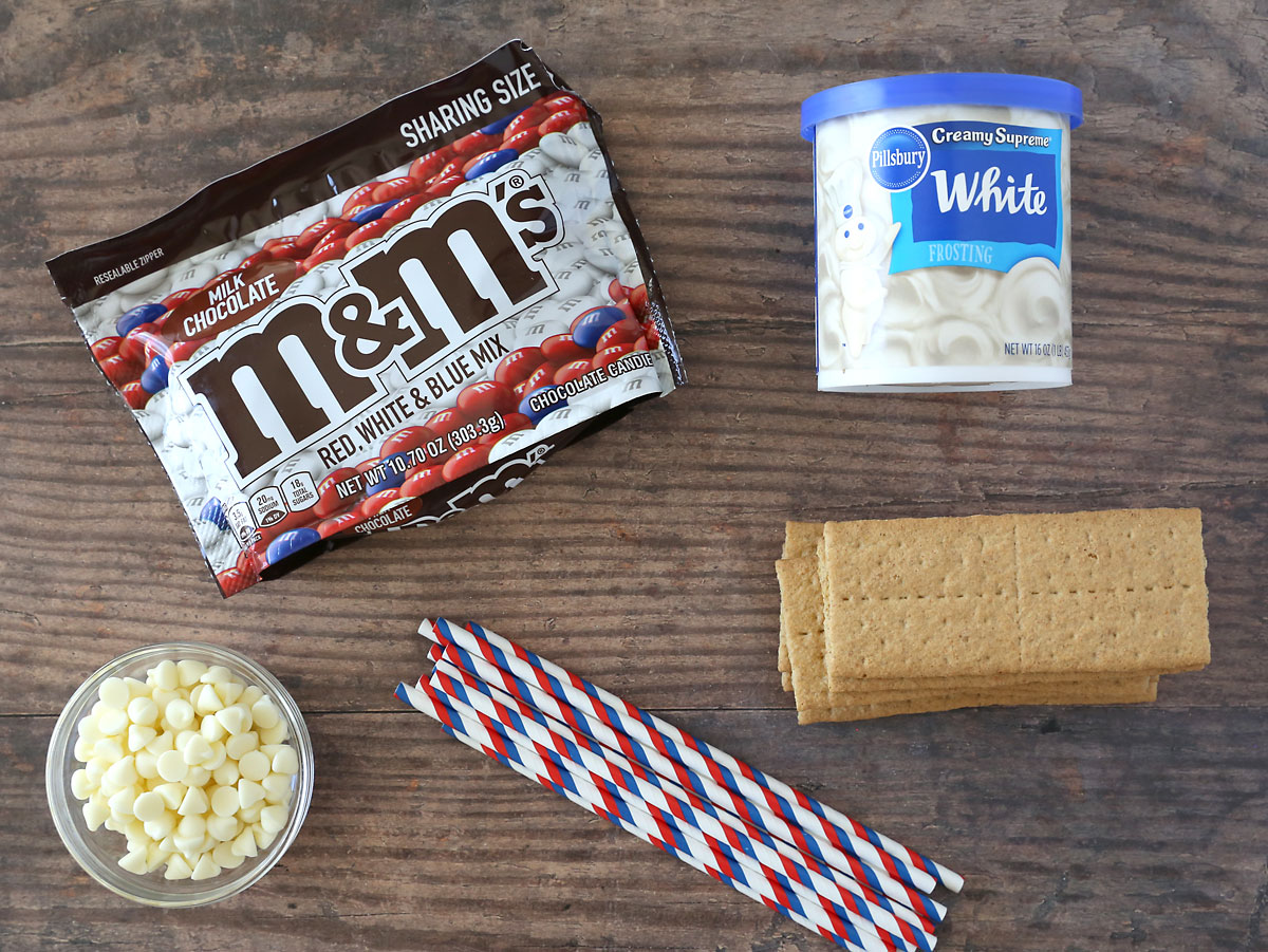 Graham cracker flag ingredients: M&Ms, graham crackers, frosting, white chocolate chips, straws