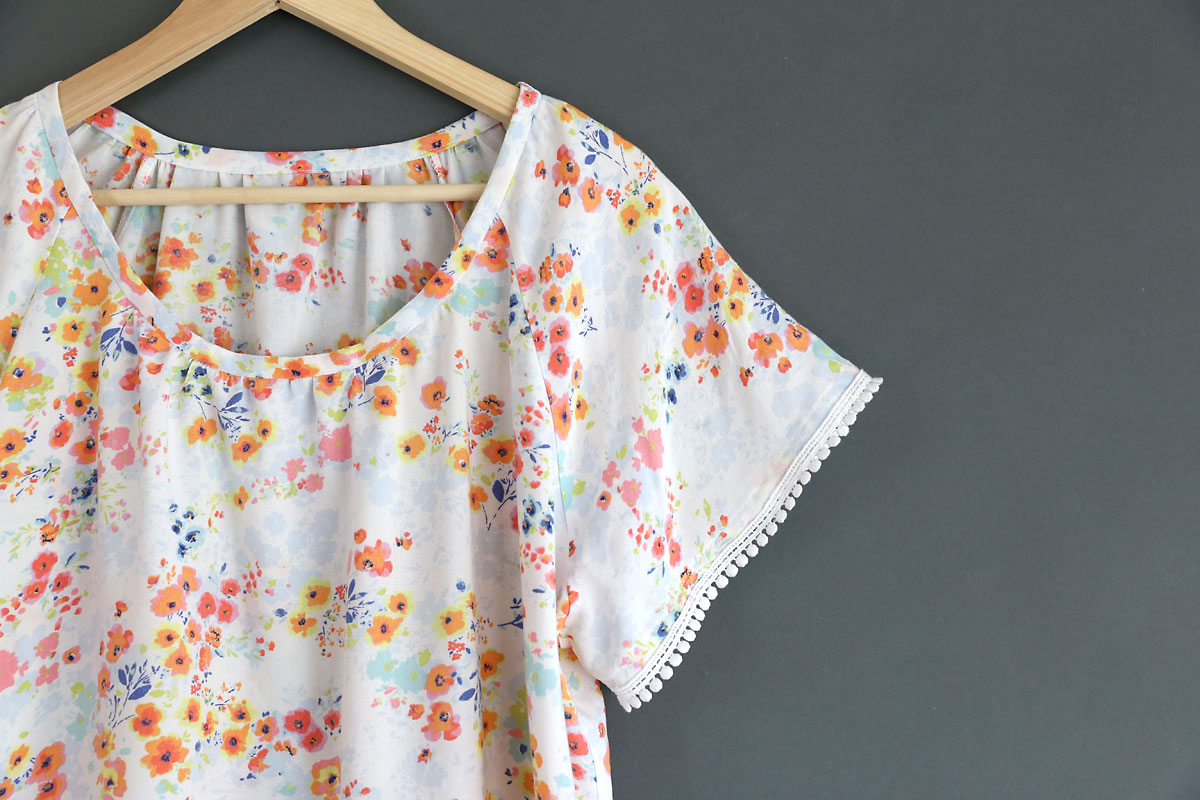 A closeup of a handsewn blouse with pink flowers and white pom pom trim on the sleeve