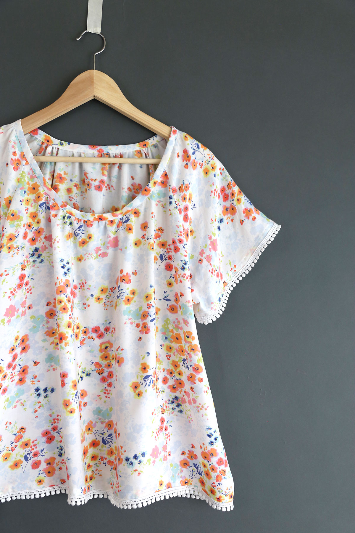 A close up of a handmade blouse with pink flowers and pom pom trim