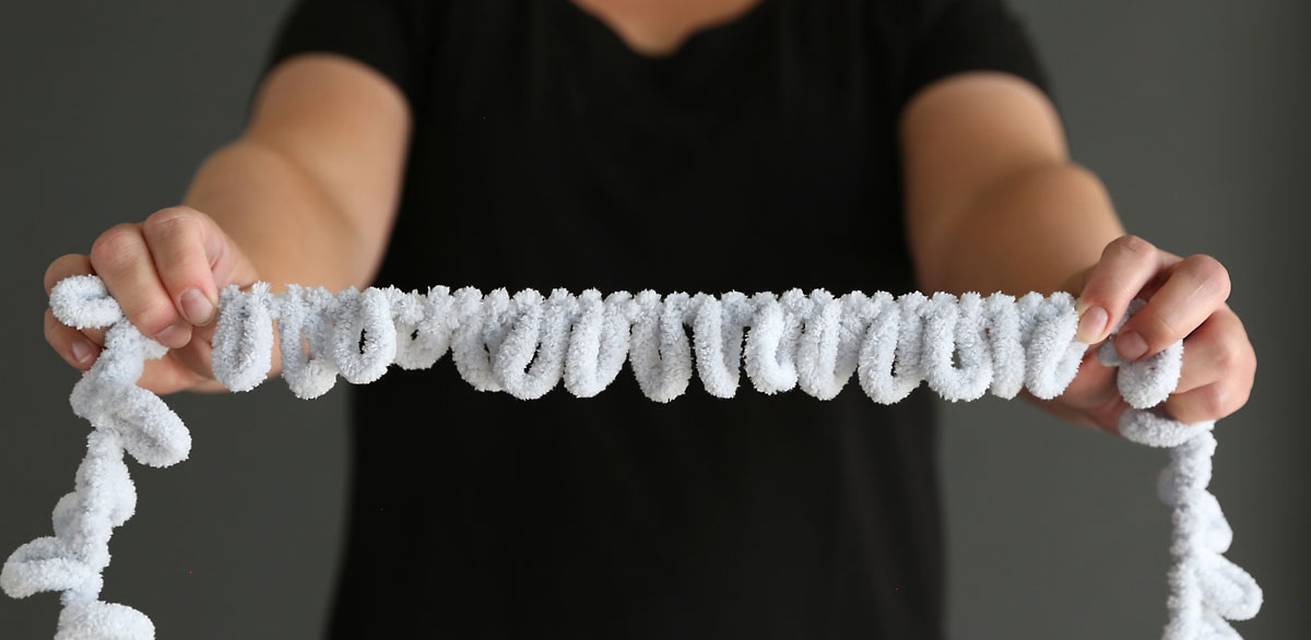A woman holding up a length of light grey loop yarn