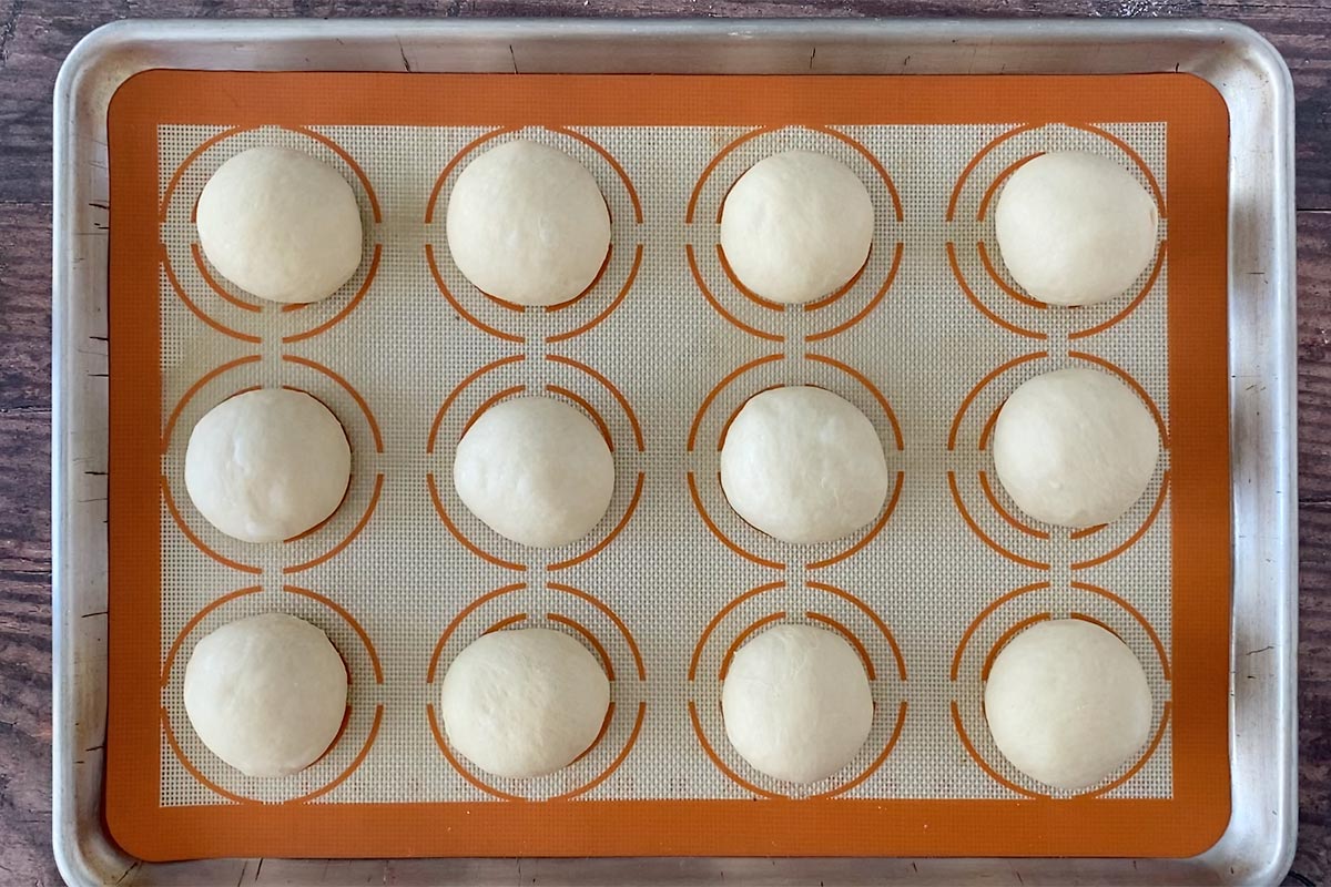 12 balls of bread dough rising on a baking sheet