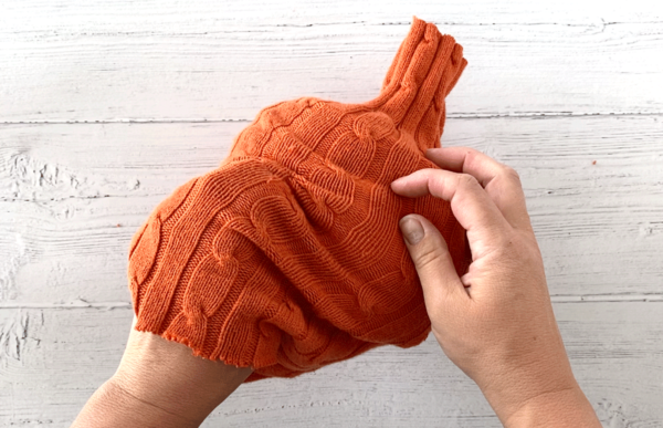 Hands placing a sweater sleeve over a roll of toilet paper to make a sweater pumpkin