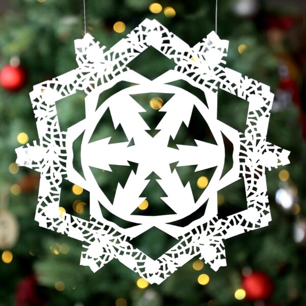 Snowflake cut from paper doily in front of a Christmas tree