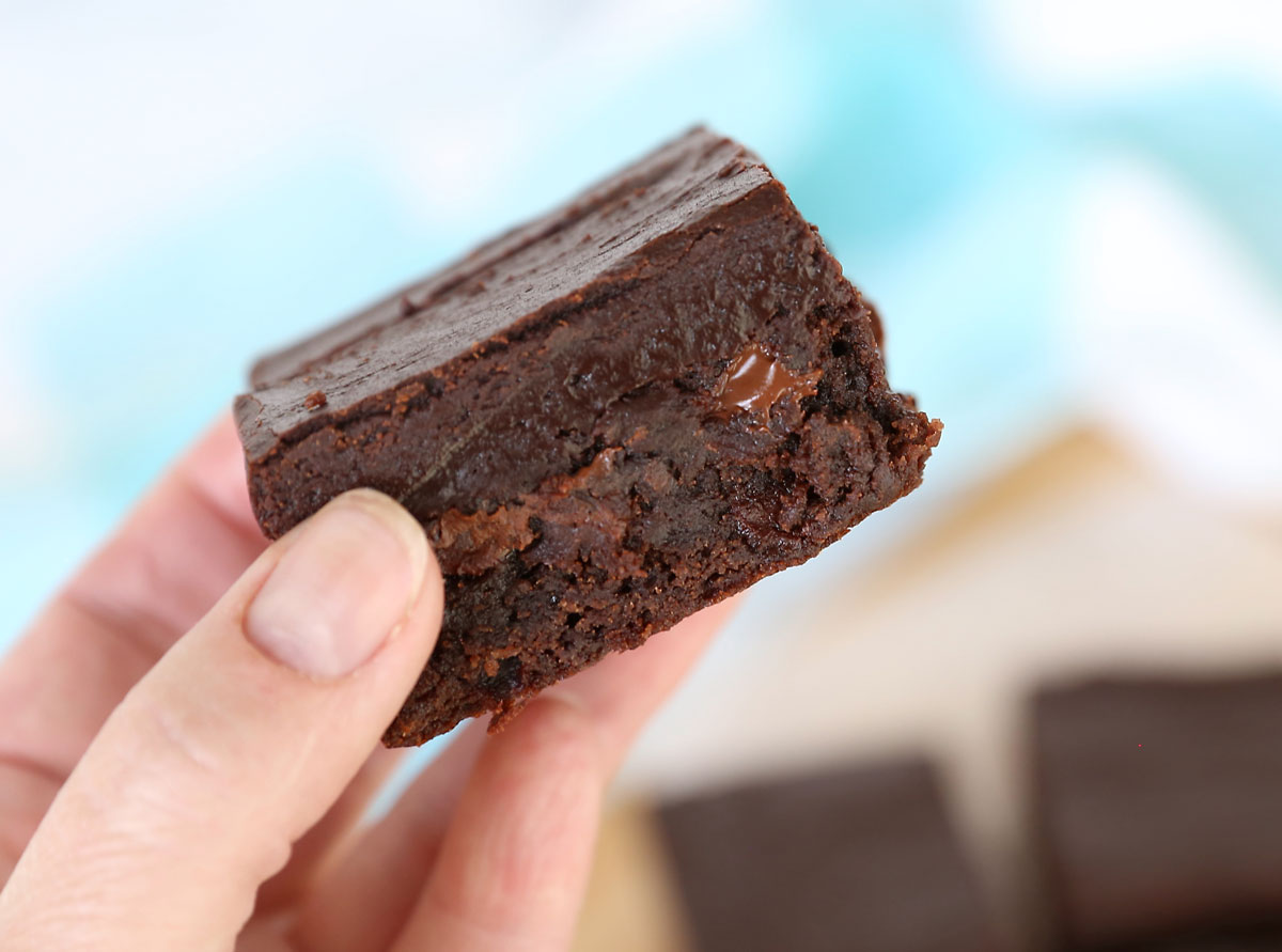 Hand holding a brownie with chocolate chips and fudge frosting