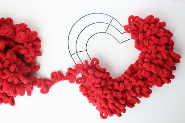 Red loop yarn covers most of the heart shaped wreath form