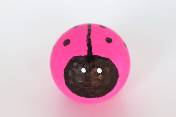 Golf ball painted pink with face drawn in black sharpie and black line and dots on the top