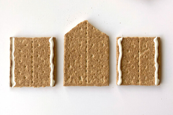 Roof support graham cracker in the center with a cracker half on either side; cracker halves both have melted white chocolate piped down either side