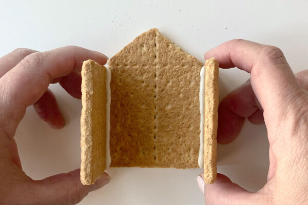 Hands holding graham cracker pieces together to form a house
