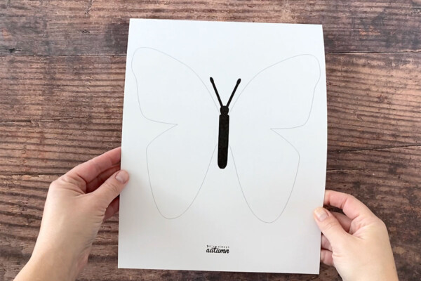 Hands holding white cardstock with butterfly outline printed on it