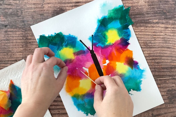 Hands using a toothpick to remove the tissue paper, leaving color behind