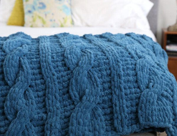 Blue handmade cable knit blanket on a bed