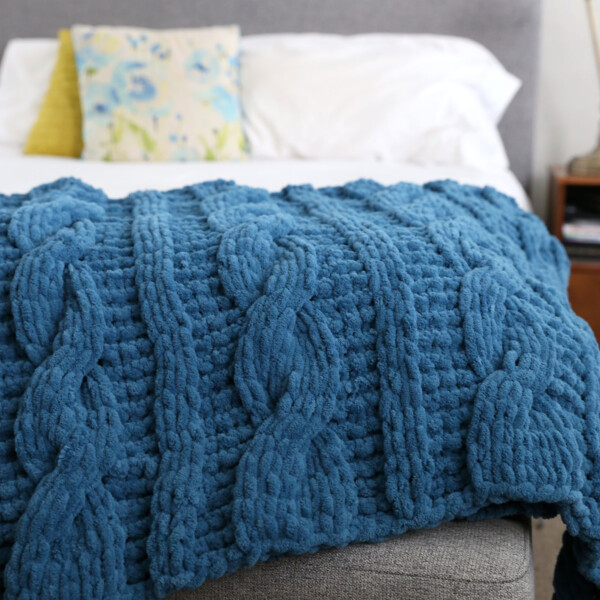 Blue handmade cable knit blanket on a bed