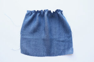 Square of blue chambray fabric that's been gathered across the top with one line of elastic thread