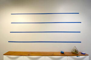Wall in a hallway with blue painters tape marking four horizontal rows