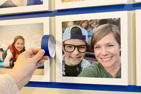 Hand holding up a roll of painters tape to measure the space in between two photo boards