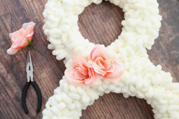 Closeup of bunny wreath with faux flowers added at the neck; pliers