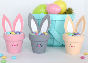 Three flower pot bunnies filled with Easter candy in front of an Easter basket